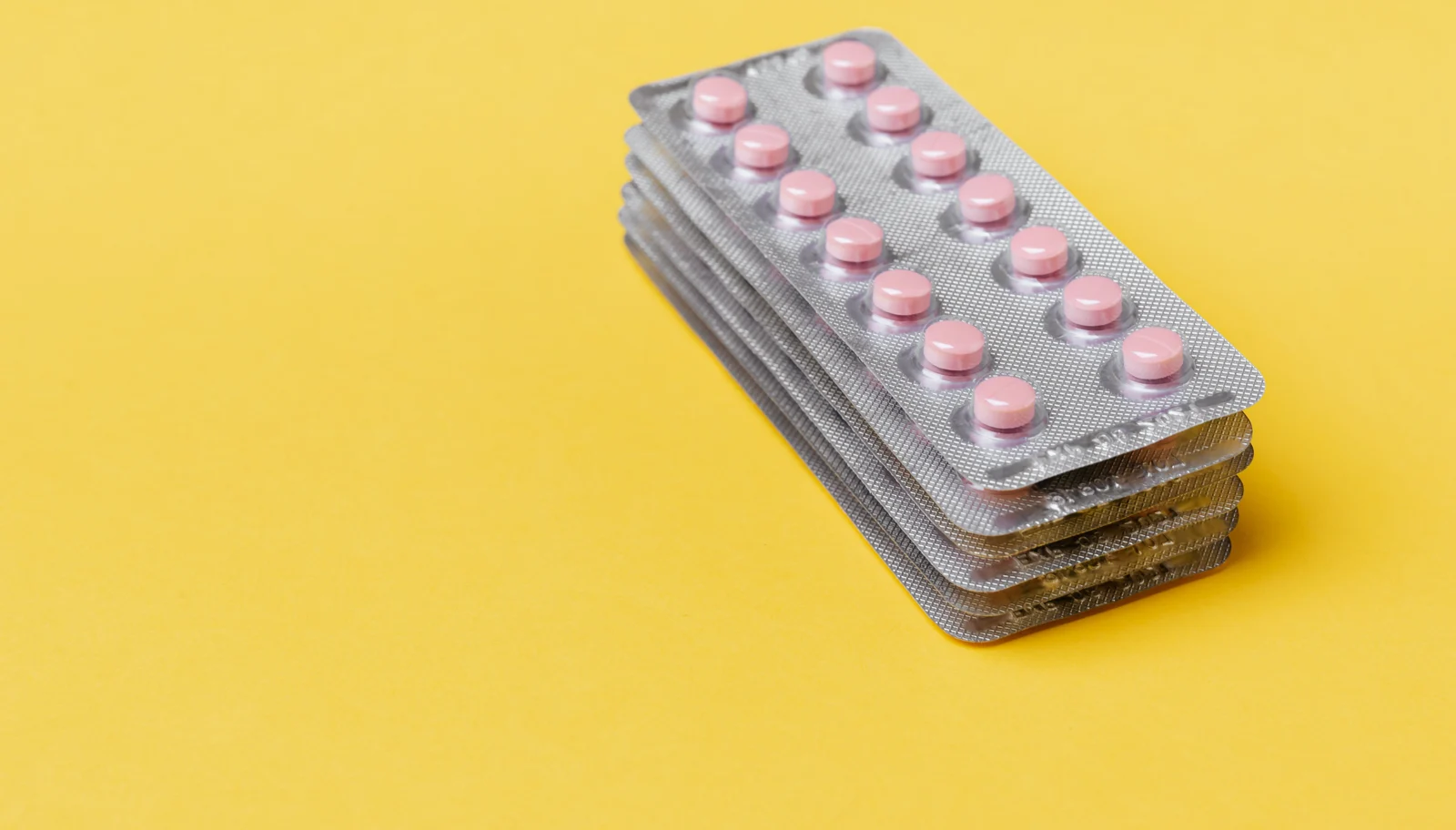 Stack of blister-packed supplement pills on a yellow background
