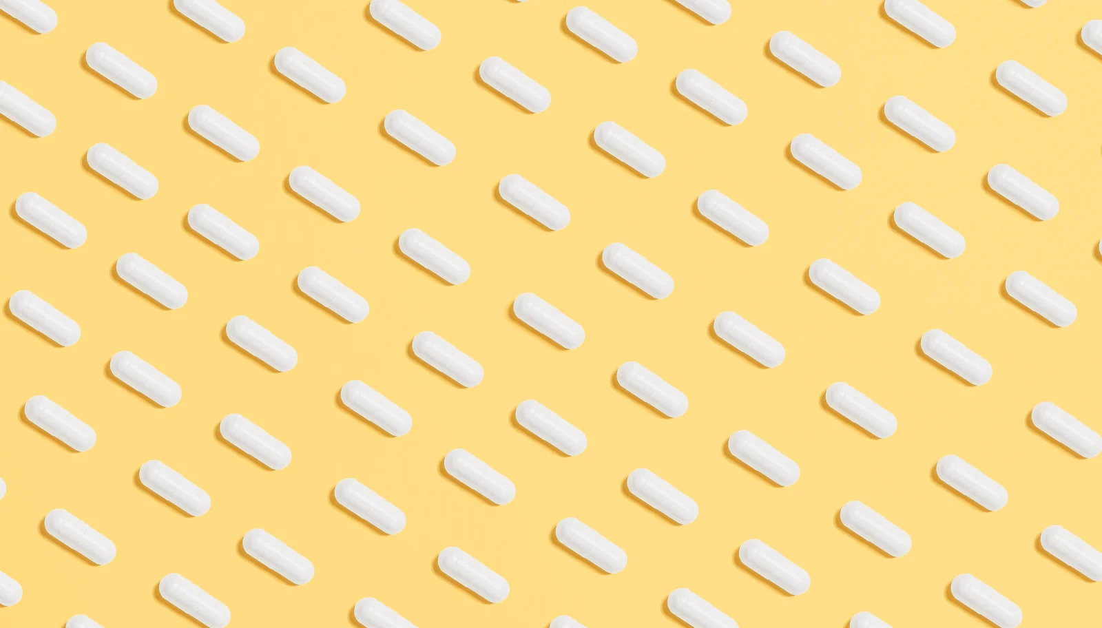 White supplement capsules arranged on a yellow background