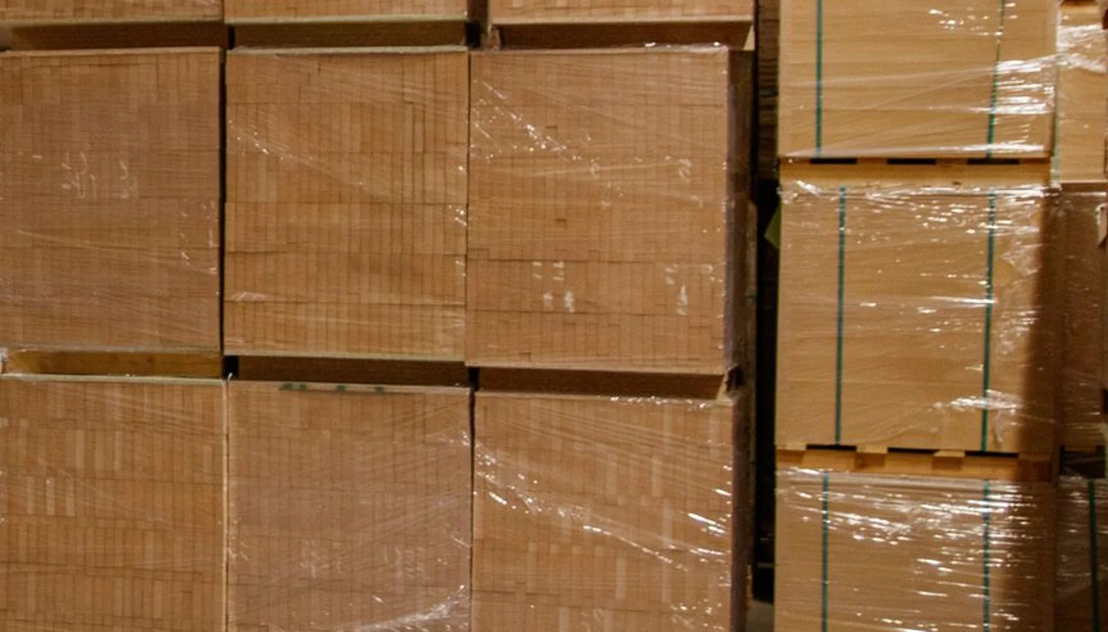 Stacks of plain shipping cartons wrapped in clear plastic on wooden warehouse pallets.