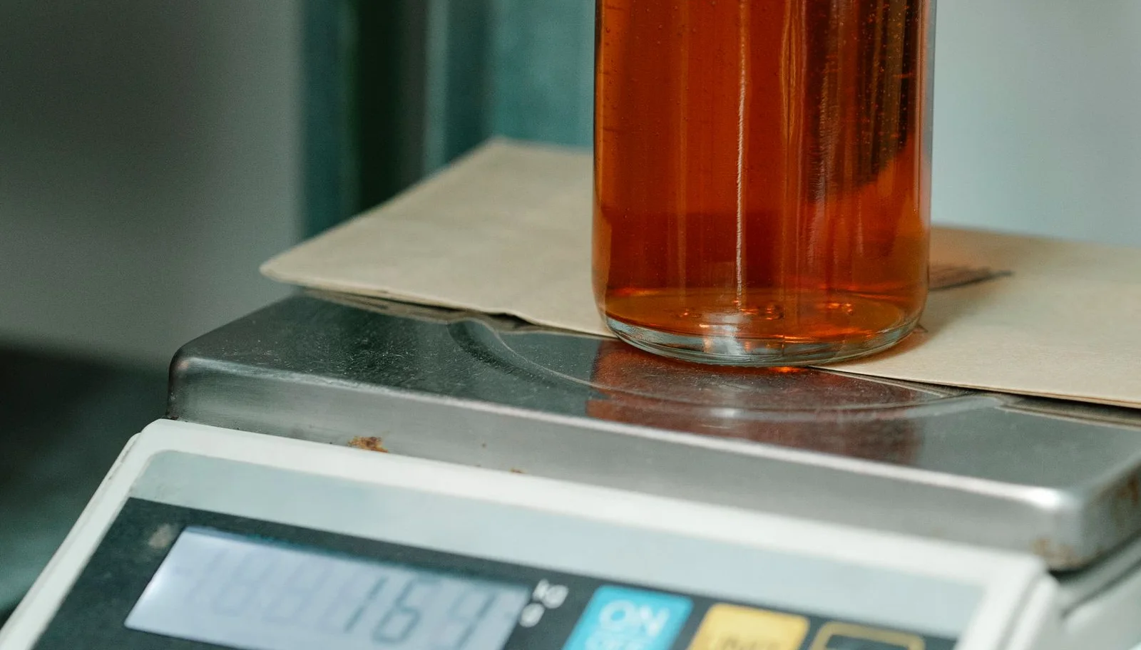 A glass bottle of amber liquid resting on a digital weighing scale during a weight check.