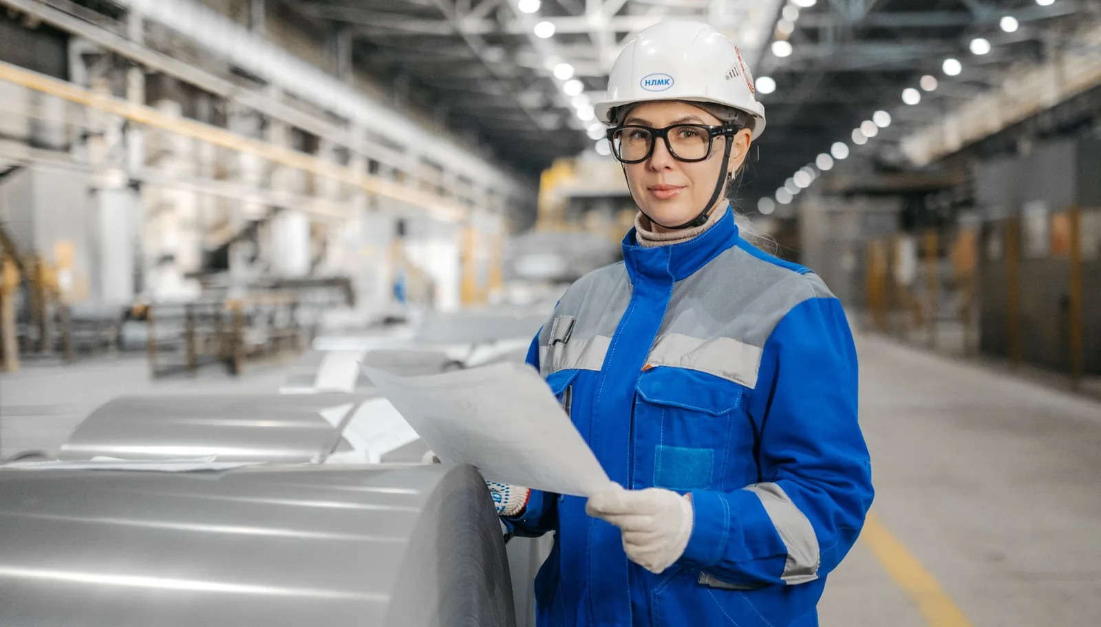 Engineer in a hard hat and safety goggles checking production equipment with documents in a factory