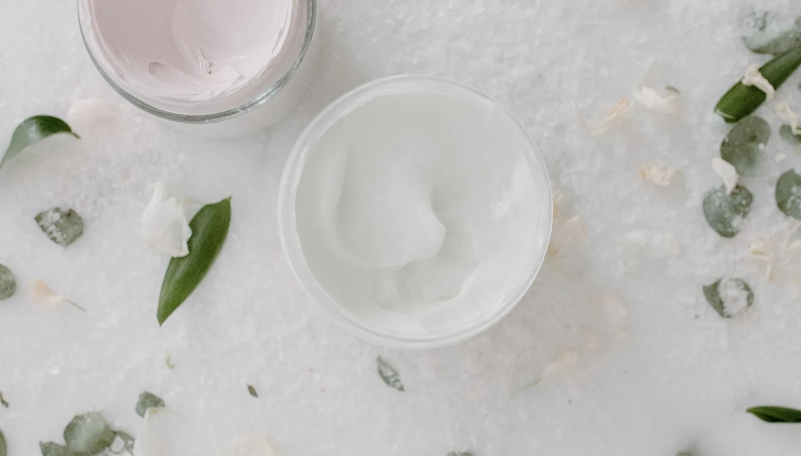 Unlabeled cosmetic cream jars with green leaves on a marble surface