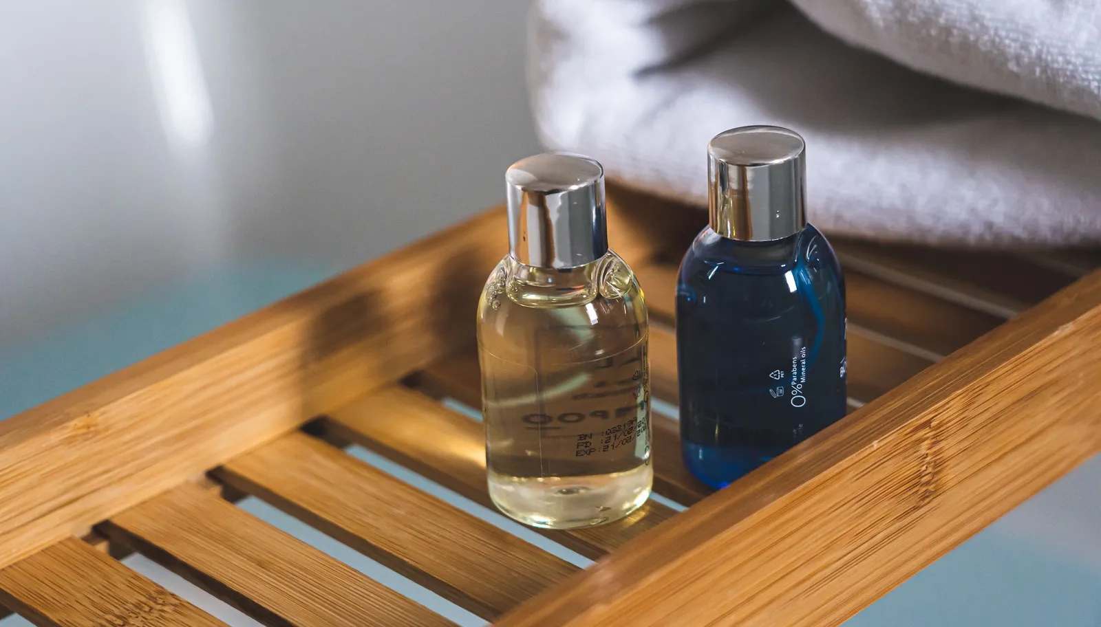 Two glass amenity bottles on a wooden tray in a hotel bathroom