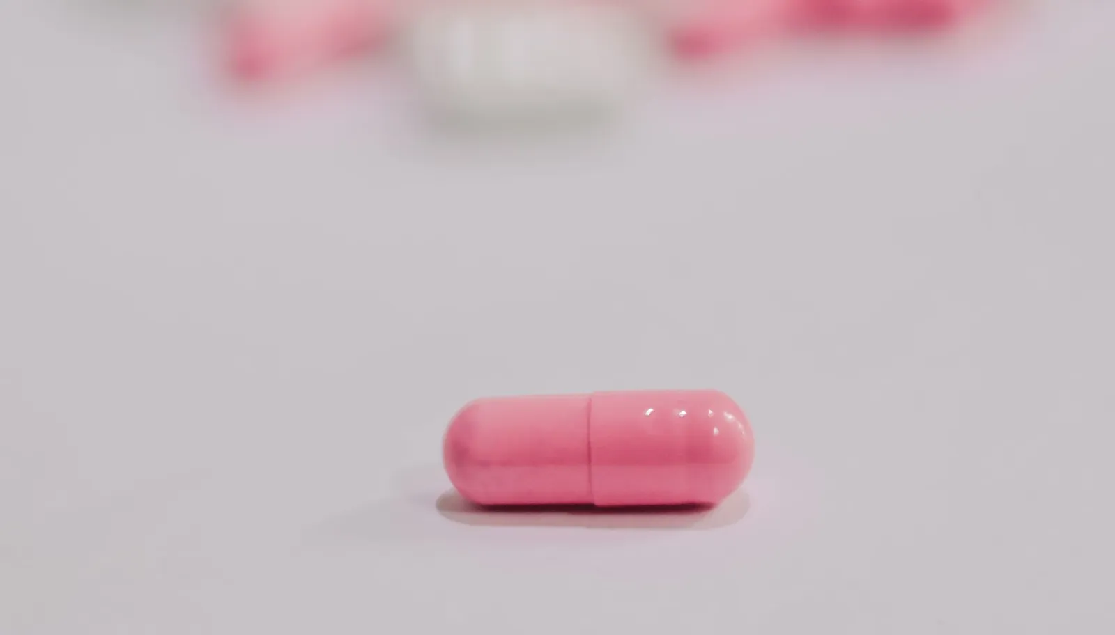 Pink and white supplement capsules scattered on a white surface