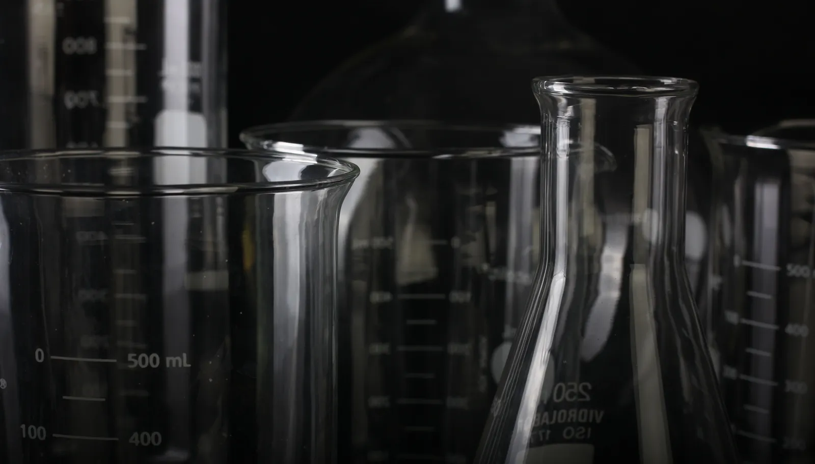 Clear laboratory beakers and flasks with graduated volume markings on a dark lab bench